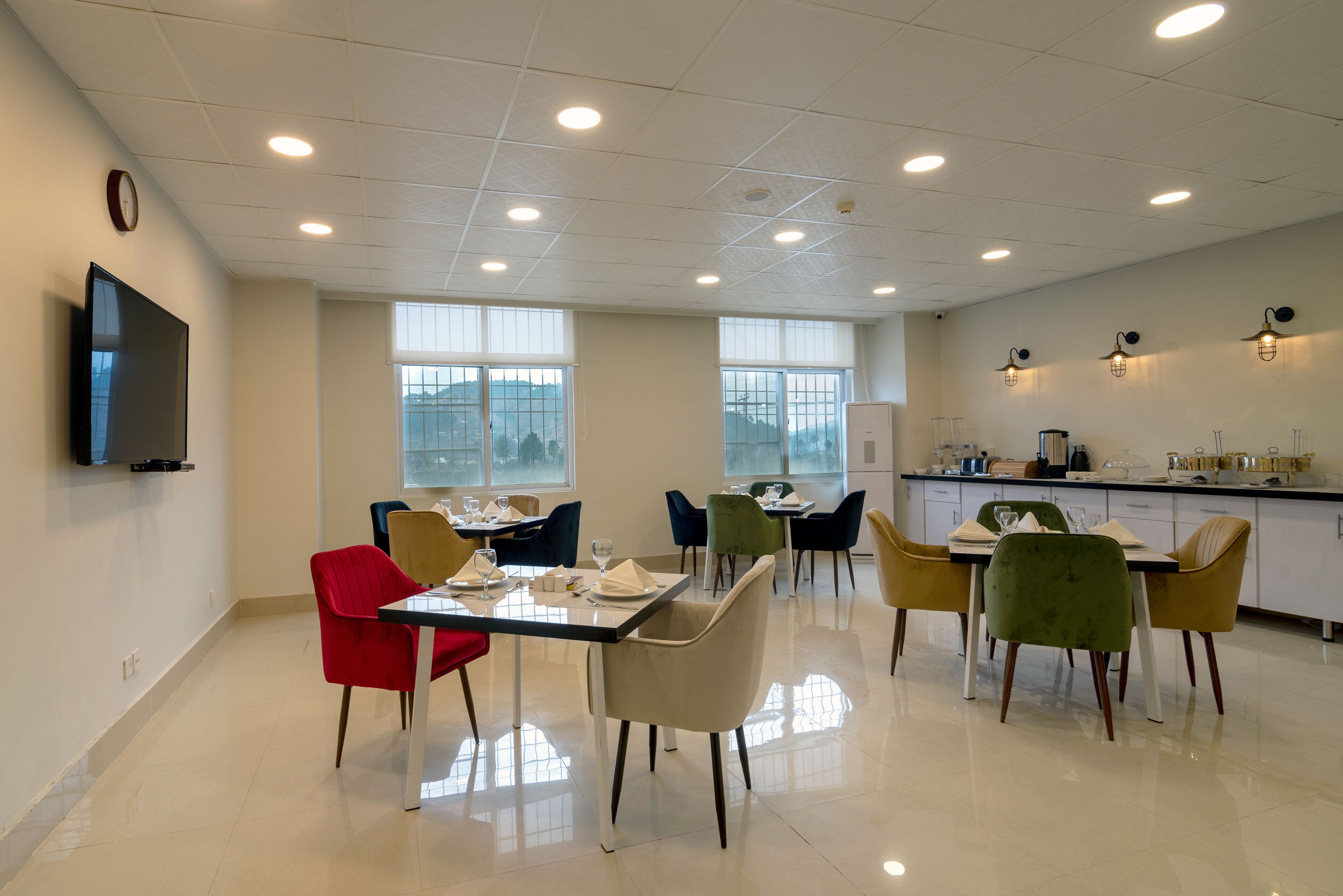 Een moderne eetruimte met een grote tafel, meerdere stoelen en een keuken met een aanrecht en apparatuur.