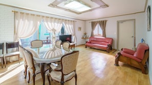 A living room with a glass dining table, wooden chairs, a red sofa, and a television. - Namhae Capetown (Namhae)