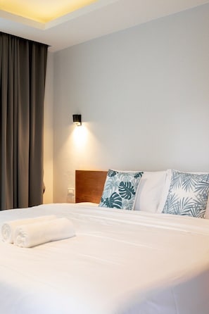 A hotel room with a neatly made bed, a headboard, a wall-mounted light, and a window with curtains.