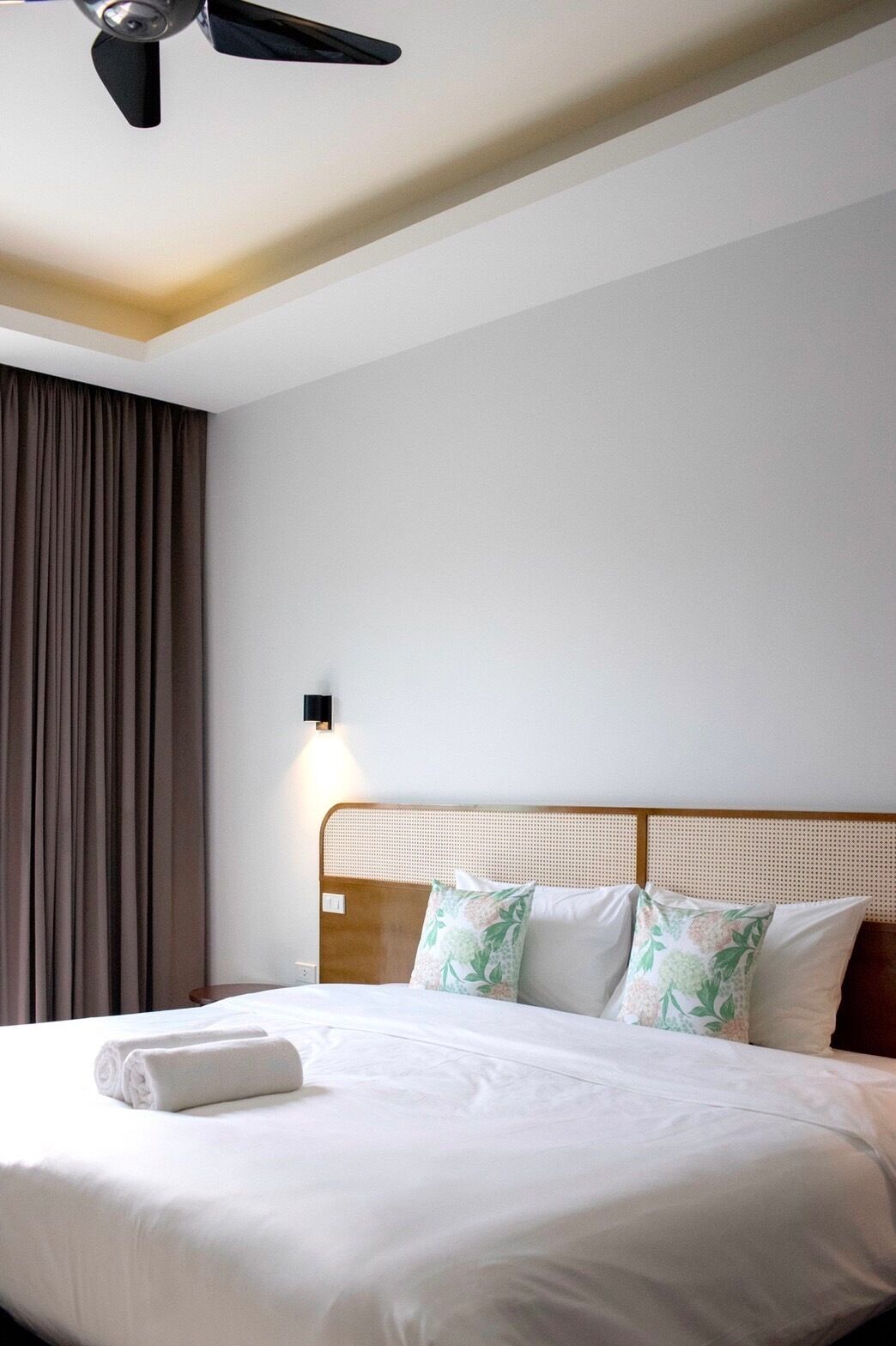 A hotel room with a bed, a ceiling fan, and a wall-mounted light fixture.