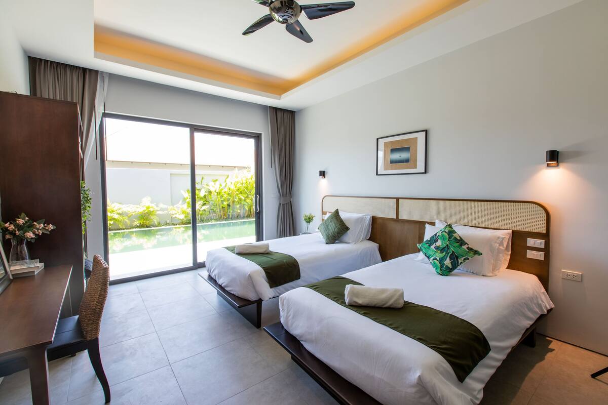 Habitación de hotel con dos camas, un escritorio y vista a un jardín a través de una puerta corrediza.