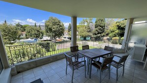 A balcony with a table and chairs, a view of a park and buildings, and a glass door. - 3-room apartment near the sea - luxury residence (Mandelieu-la-Napoule)