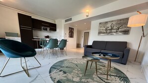 A modern living room with a grey sofa, teal chairs, a glass coffee table, and a patterned rug. - 3-room apartment near the sea - luxury residence (Mandelieu-la-Napoule)