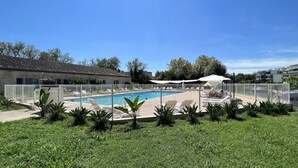 A swimming pool with lounge chairs and a covered area, surrounded by a white fence and greenery. - 3-room apartment near the sea - luxury residence (Mandelieu-la-Napoule)