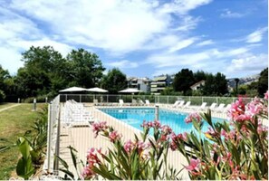 A swimming pool with lounge chairs and umbrellas, surrounded by greenery and buildings in the background. - 3-Bedroom Apartment Near the Ocean - Luxury Residence (Mandelieu-la-Napoule)