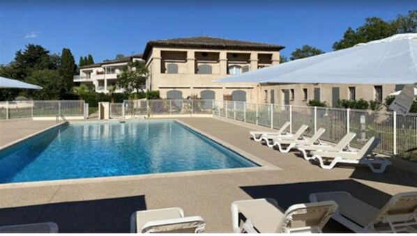 A swimming pool with lounge chairs, a fence, and a building in the background. - 3-Bedroom Apartment Near the Ocean - Luxury Residence (Mandelieu-la-Napoule)