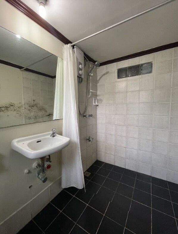 Un baño con lavamanos blanco, ducha y suelo de baldosas.