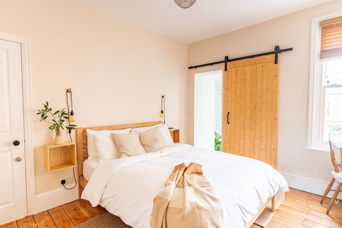 Quarto com cama de madeira, uma planta na mesa de cabeceira, porta deslizante e janela com persianas.