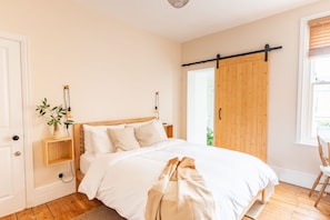 A bedroom with a wooden bed, a bedside plant, a sliding door, and a window with blinds. - Doghouse Margate (Margate)