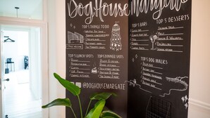 Een schoolbord met een welkomstbord voor DogHouse Margale, waarop de vijf beste activiteiten, lunchplekken, dinerplekken, bars, desserts en wandelingen met de hond staan vermeld.