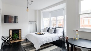Een moderne slaapkamer met een groot bed, een aan de muur bevestigde televisie, een open haard en een eethoek met een tafel en stoelen.