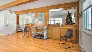 A spacious room with wooden floors, a wooden reception desk, two chairs, a small table, and a Christmas tree. - Cozy Postville Retreat w/ Fireplaces & Yard! (Postville)