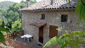 A stone house with a tiled roof, a small porch with a table and chairs, and a wooden fence. - Gîte in an Ardéchois farmhouse in the heart of nature (Fabras)