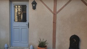 A building facade with a white door, a potted plant, and a mailbox.