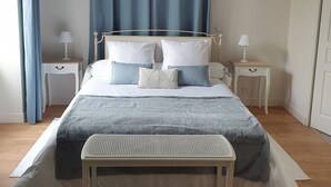 A neatly arranged bedroom with a bed, bedside tables, a bench, and a painting on the wall.