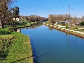 A calm river with grassy banks and a few buildings along the side.