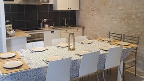 A dining area with a table set for four, a kitchen in the background, and a stone wall.