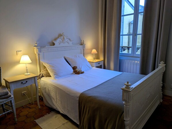 A neatly made bed with white linens, a teddy bear, and two bedside lamps.