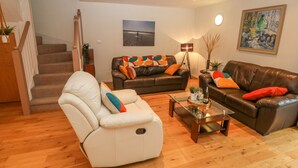 A living room with a white recliner, two leather sofas, a coffee table, and a staircase. - Barn End, 9 Stad Clynnog (Llanfairpwllgwyngyll)