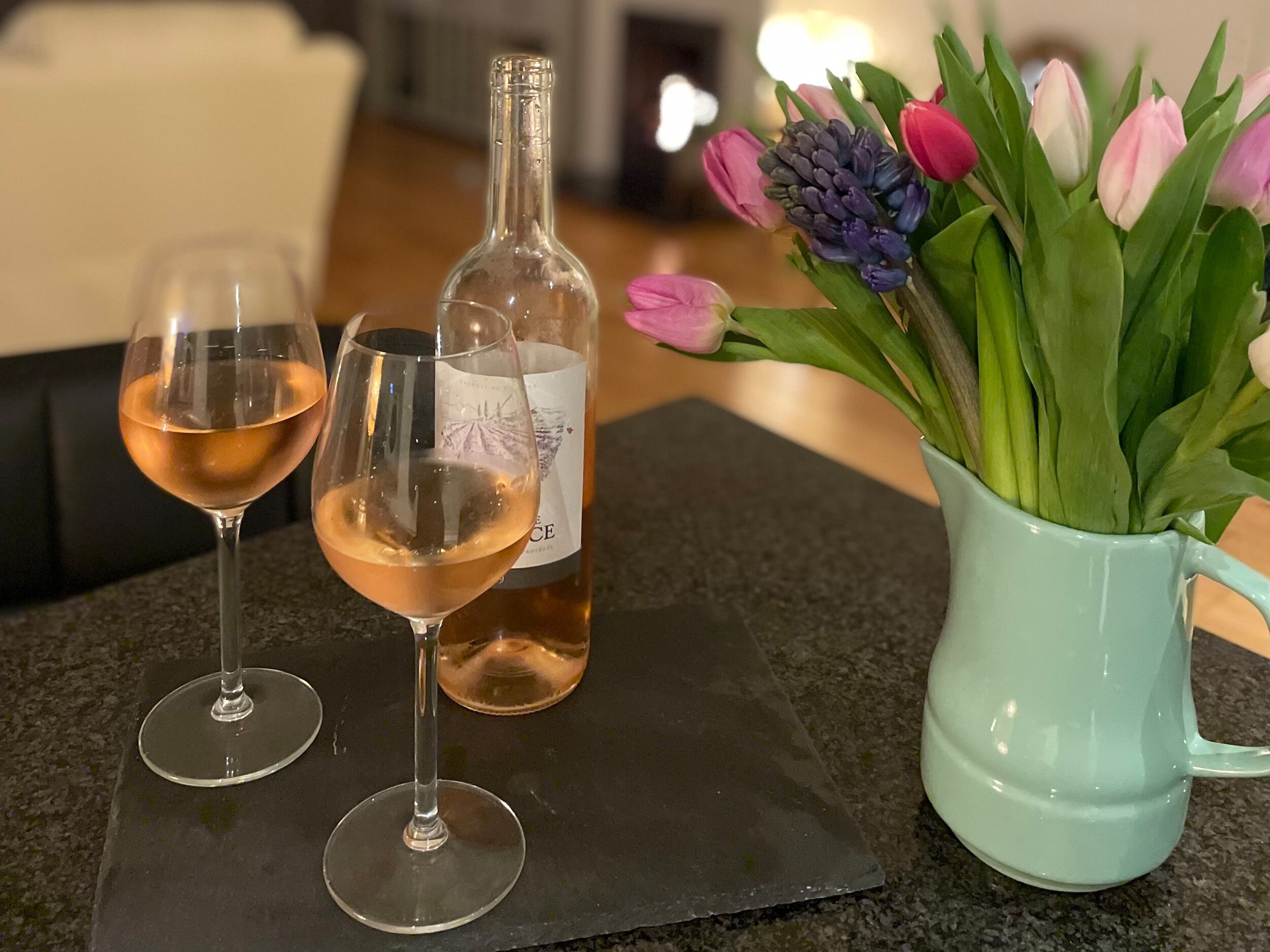 Two wine glasses on a black mat, a bottle of wine, and a vase with tulips.