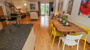 A modern kitchen with a granite countertop, wooden dining table, and yellow chairs. - Barn End, 9 Stad Clynnog (Llanfairpwllgwyngyll)