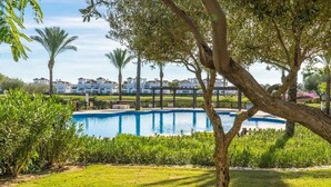 A swimming pool surrounded by lush greenery and palm trees, with a view of white buildings in the background. - Villa in La Torre Golf Resort. pet friendly (Torre-Pacheco)