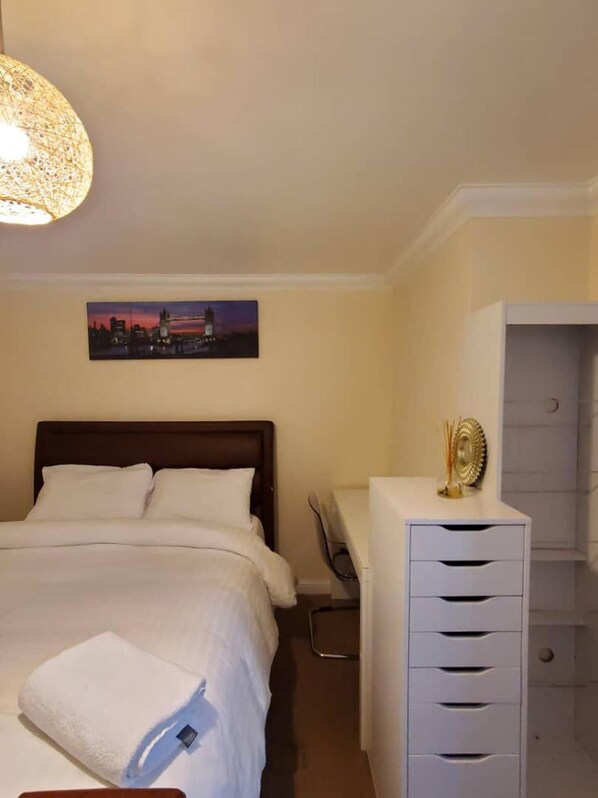 Habitación de hotel con cama, escritorio, silla, armario y un cuadro de un paisaje urbano.