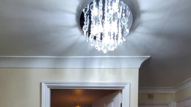 Quarto com cama, lustre e porta que dá para outro cômodo.