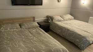 Une chambre avec deux lits simples, un téléviseur fixé au mur et une petite table de chevet.