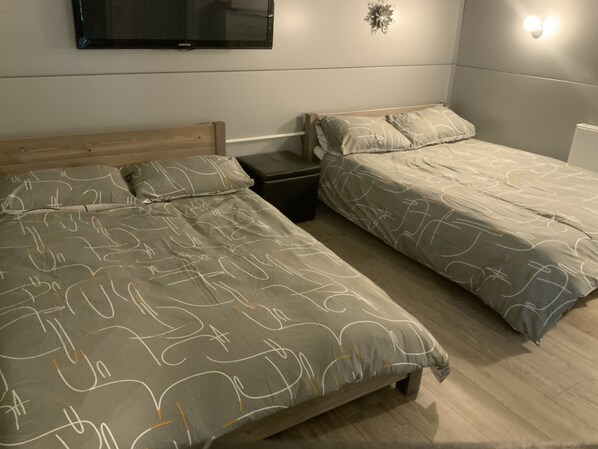 A bedroom with two single beds, a TV mounted on the wall, and a small bedside table.