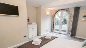 A bedroom with a bed, a dresser, a mirror, and a stone archway leading to a balcony. - The Chalet (Tyn-y-Gongl)