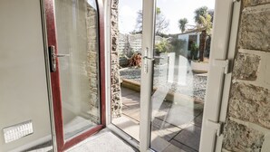A glass door leading to a courtyard with a stone wall, a wooden door, and a metal handle. - The Chalet (Tyn-y-Gongl)
