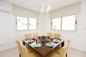 A dining room with a wooden table set for eight, beige chairs, and a chandelier.