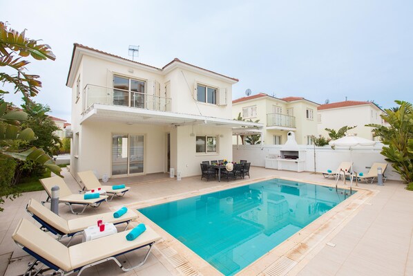 Ein zweistöckiges Haus mit Swimmingpool, Außenbereich mit Sitzgelegenheiten und einer überdachten Terrasse.