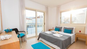 Une chambre d’hôtel moderne équipée d’un lit, d’un bureau, d’une chaise et offrant une vue sur la ville grâce à de grandes fenêtres.