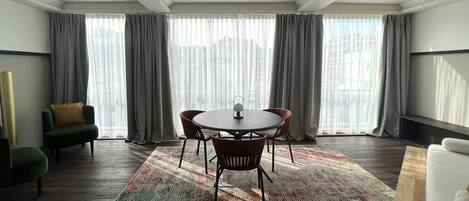 A modern room with a round table, two chairs, a sofa, and a large window with curtains.