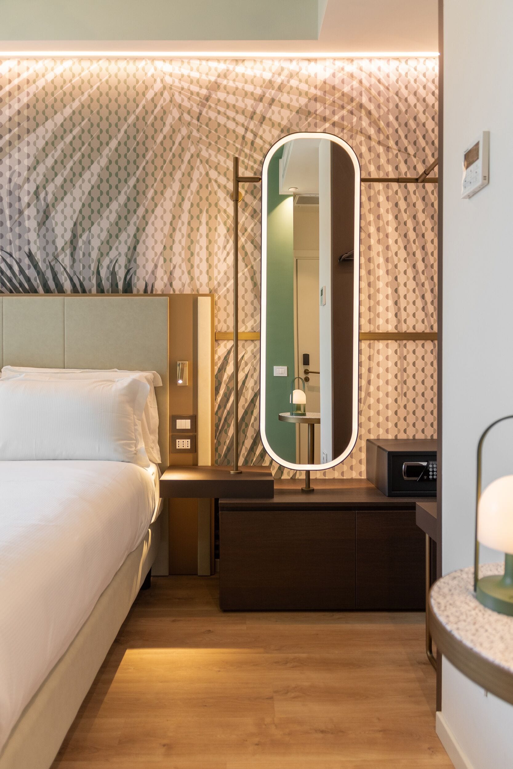 A hotel room with a bed, a bedside table with a lamp, a mirror, and a microwave.