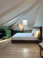 A modern loft bedroom with a sloped ceiling, a skylight, a bed with white bedding, a TV, and a green accent wall.
