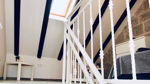 Una habitación con techo inclinado, una escalera blanca con barandilla y una pared de piedra.
