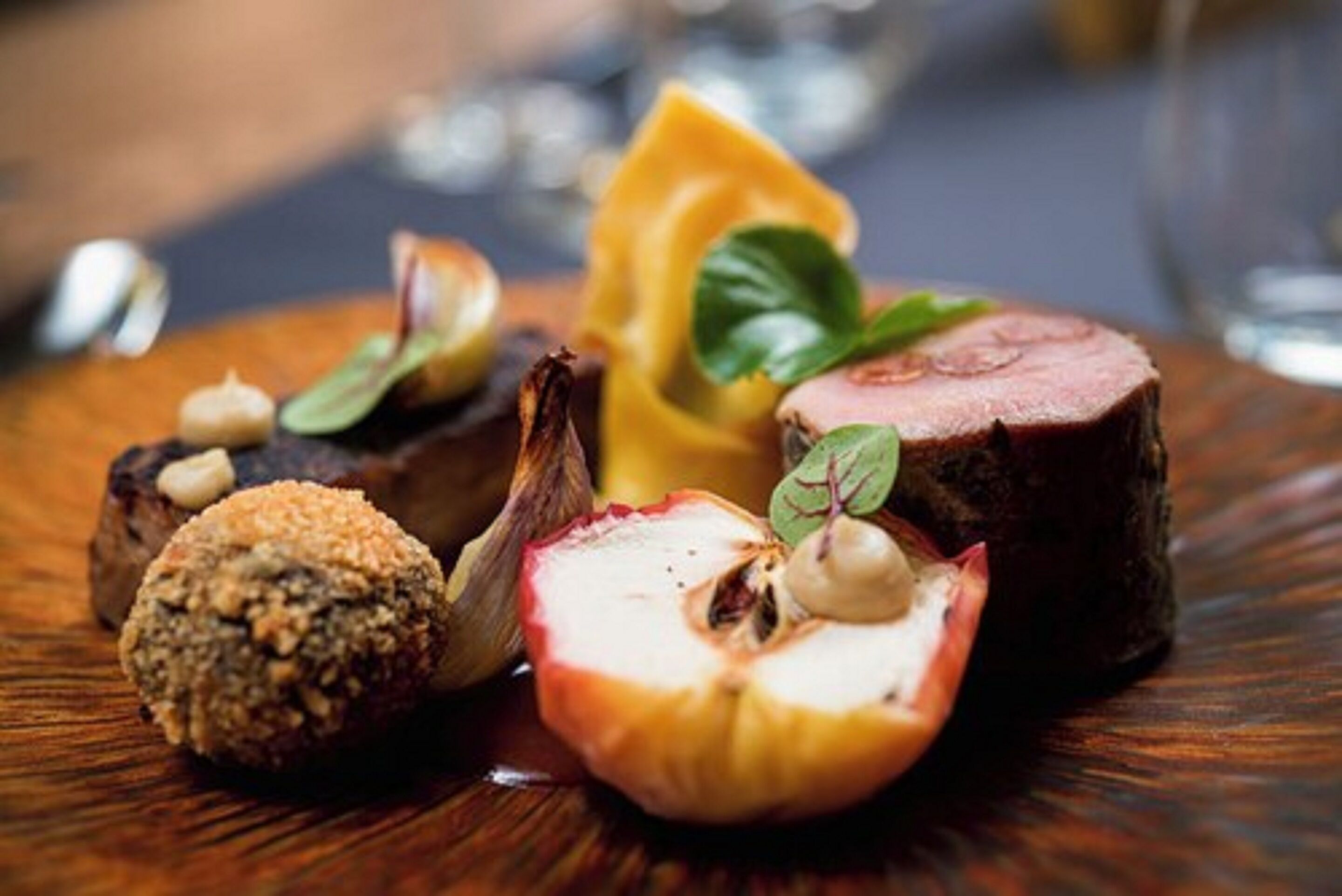 Un plato de postre con diferentes elementos, como fruta cortada, un rollo de nuez y un trozo de carne, todo sobre una superficie de madera.