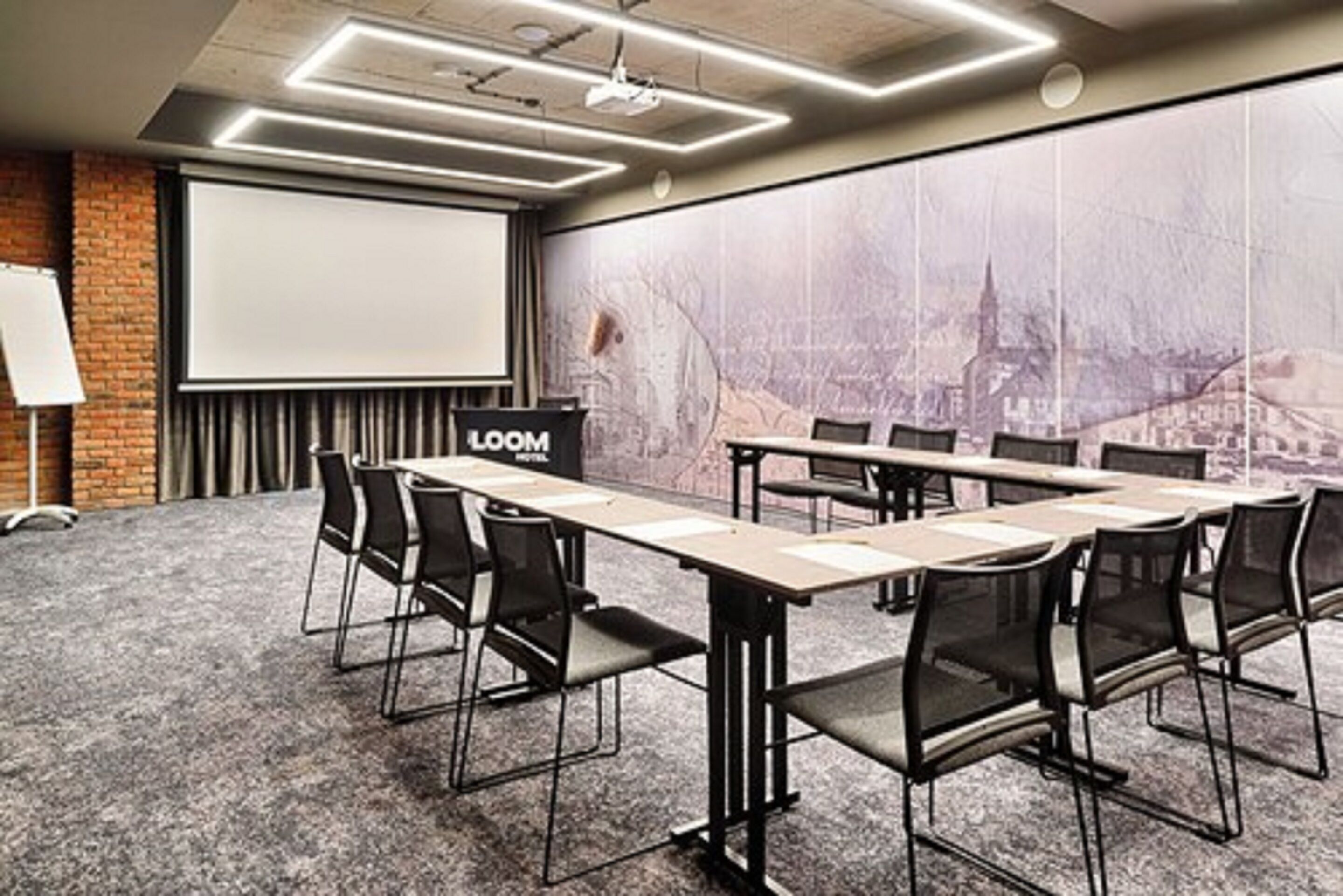 Un salón de conferencias con una larga mesa, sillas, una pantalla de proyector y un mural con vista a la ciudad.