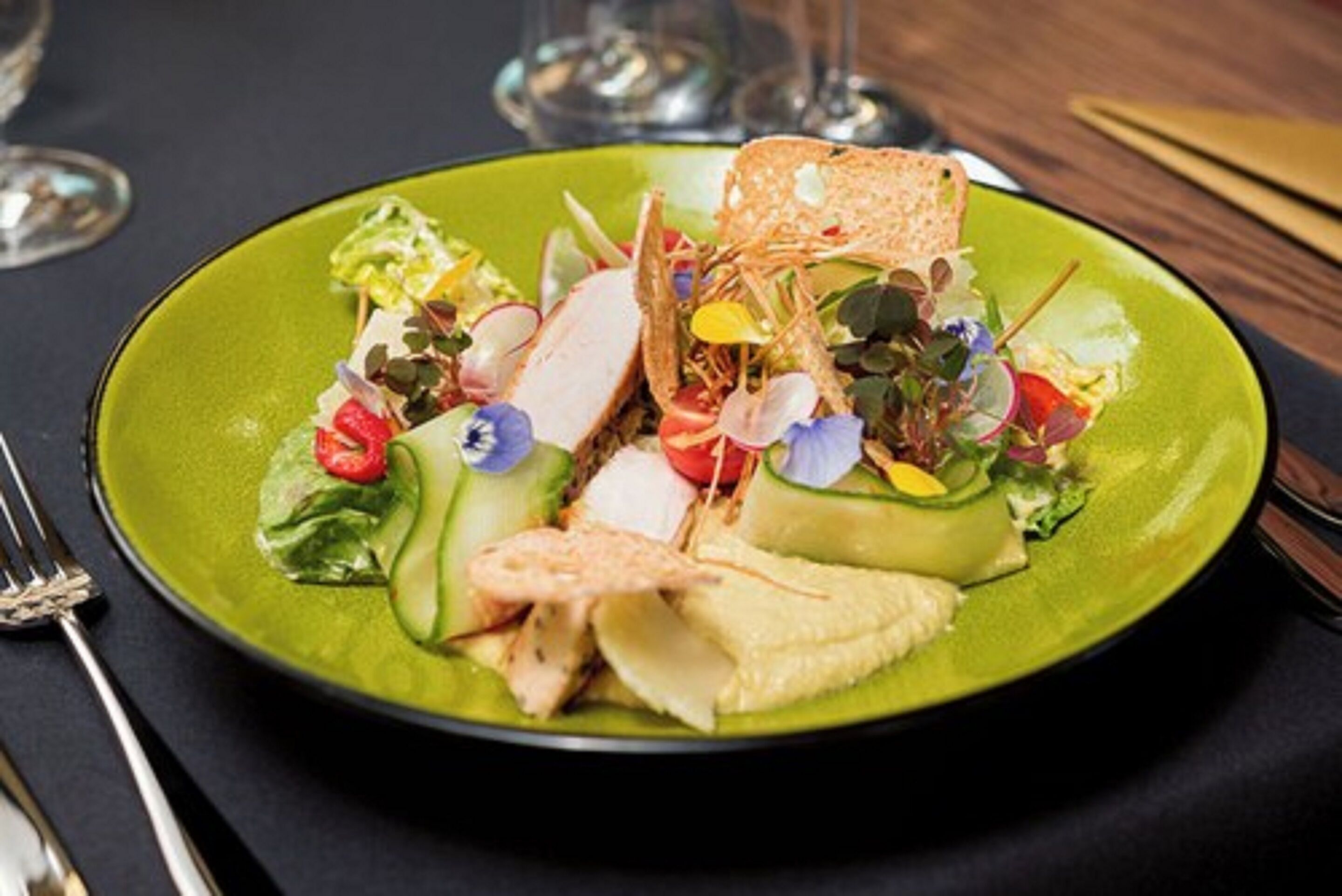A green plate with a salad, including various vegetables and a piece of bread.