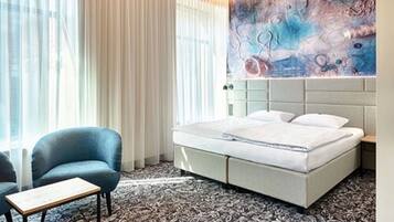 A hotel room with a bed, a chair, a small table, and a large abstract painting on the wall.