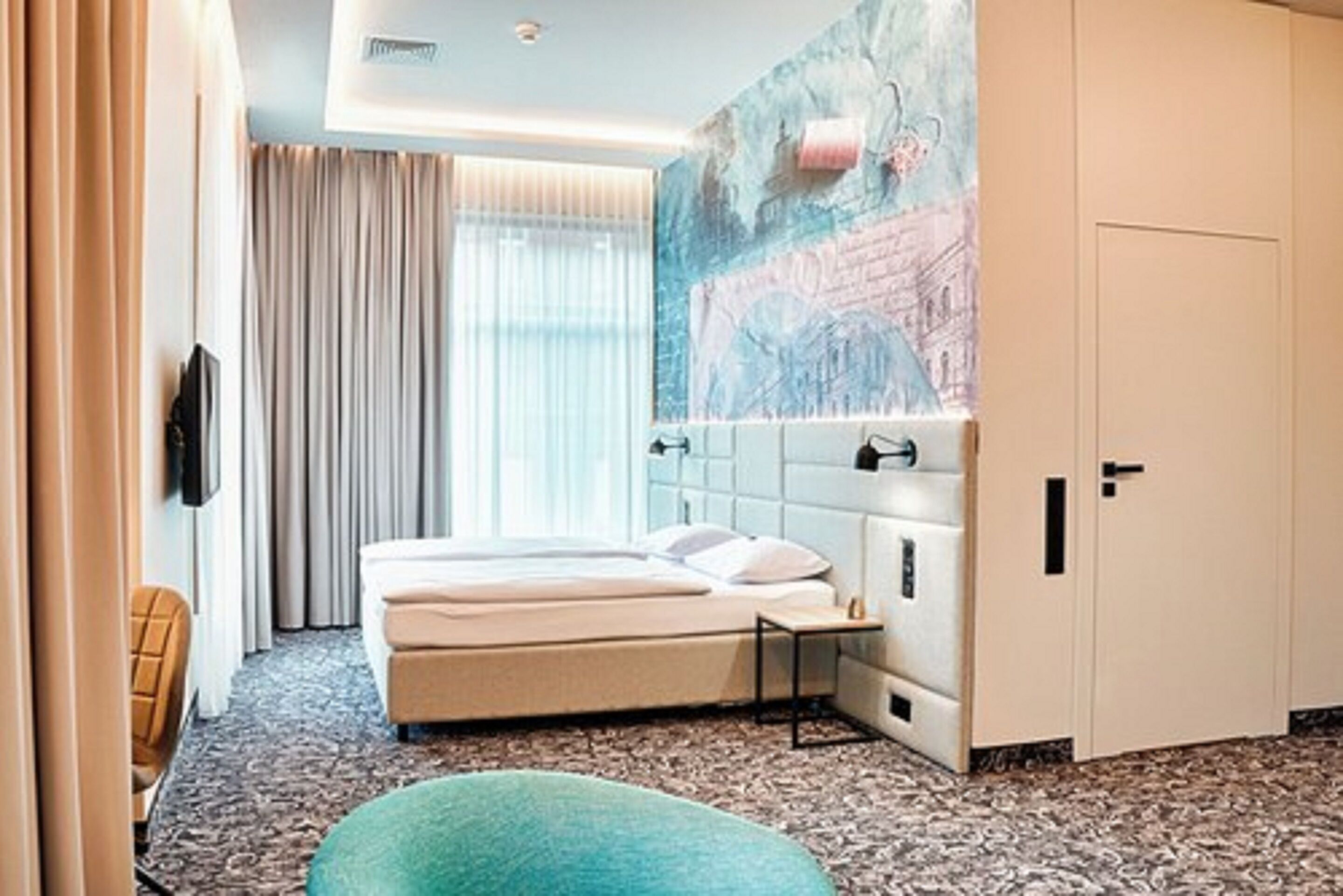 A hotel room with a bed, a headboard, a wall-mounted TV, a window with curtains, and a painting.