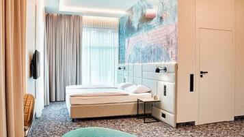 A hotel room with a bed, a headboard, a wall-mounted TV, a window with curtains, and a painting.
