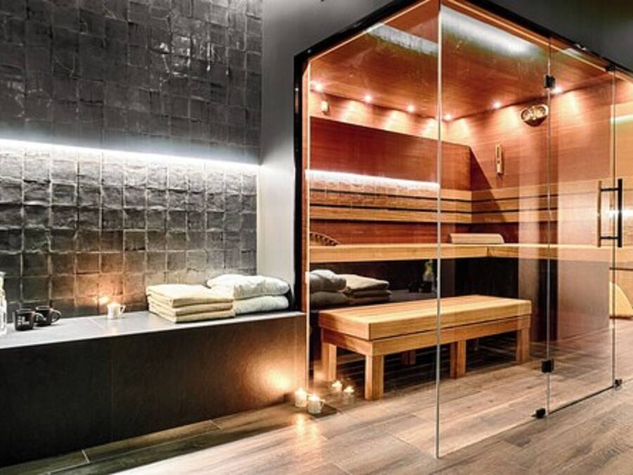 A modern sauna with glass walls, a wooden bench, and a stone wall backdrop.