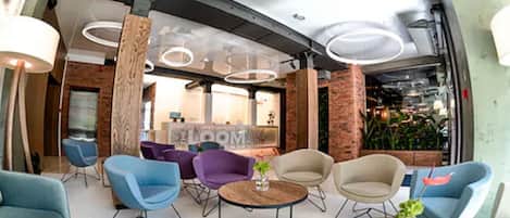 A modern lounge area with round tables, blue and purple chairs, and a brick wall backdrop.