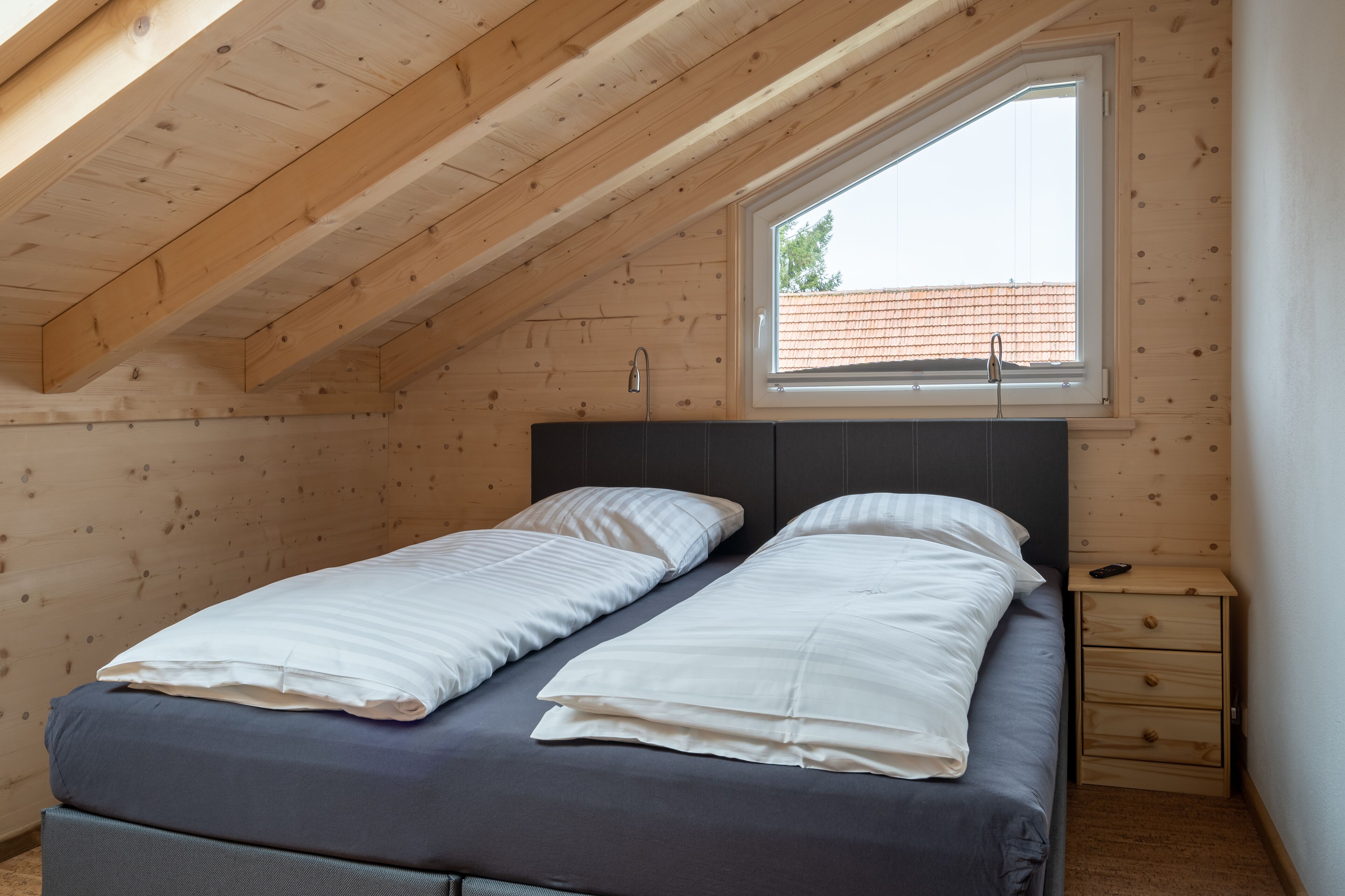 Une chambre avec deux lits, une fenêtre et une table de chevet en bois.