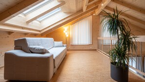 Ein Dachzimmer mit einer Couch, einer Topfpflanze und einem Fenster mit Jalousien.