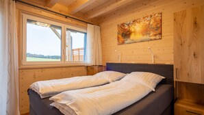 Ein Schlafzimmer mit Bett, Fenster, einem Gemälde und Holzwänden.